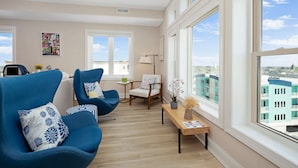 A modern living room with a large window, a sofa, a chair, a small table, and a lamp. - Penthouse in Wildwood Crest- Best Views! (Wildwood)