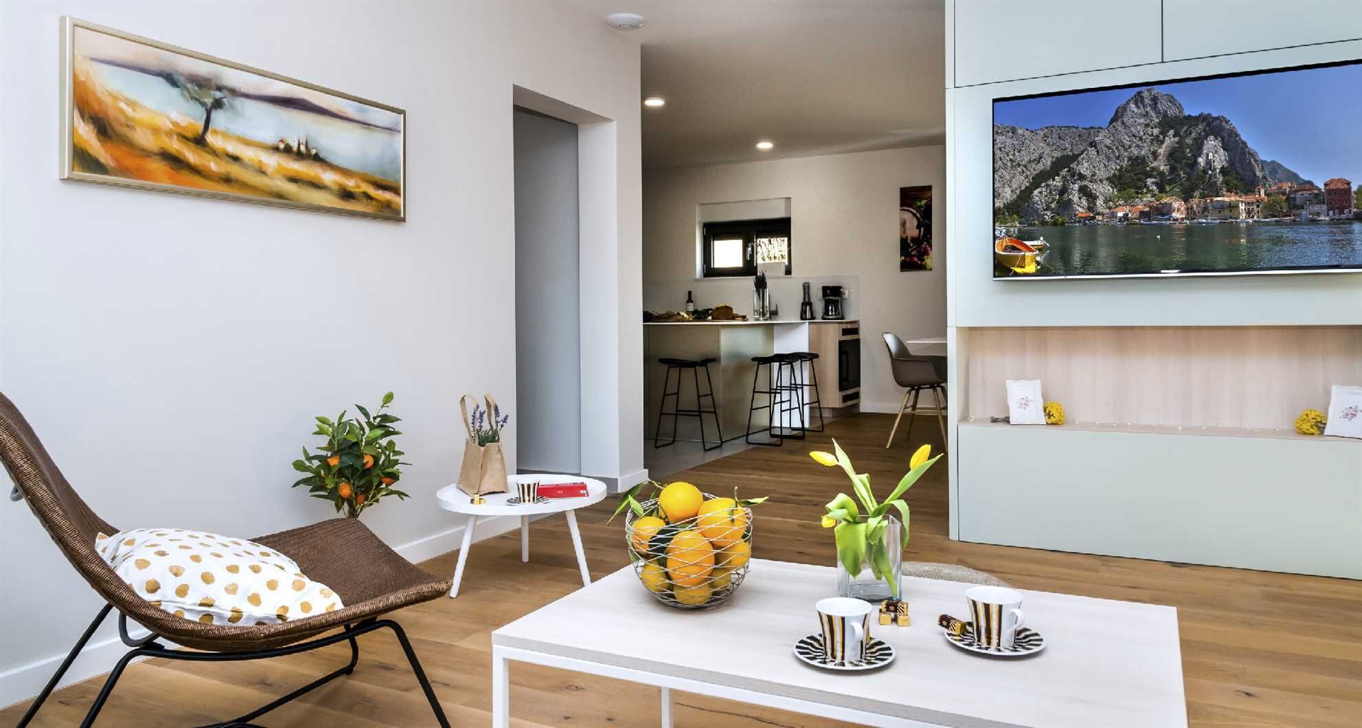 En moderne stue med spiseområde, et køkken og et tv, der viser et smukt landskab.