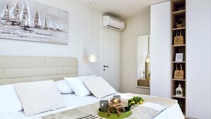 A bedroom with a bed, a painting of sailboats, an air conditioning unit, a hanging light, a mirror, and a shelf with decorative items. - Villa Luxury Dream in Omiš, indoor heated pool (Omiš)