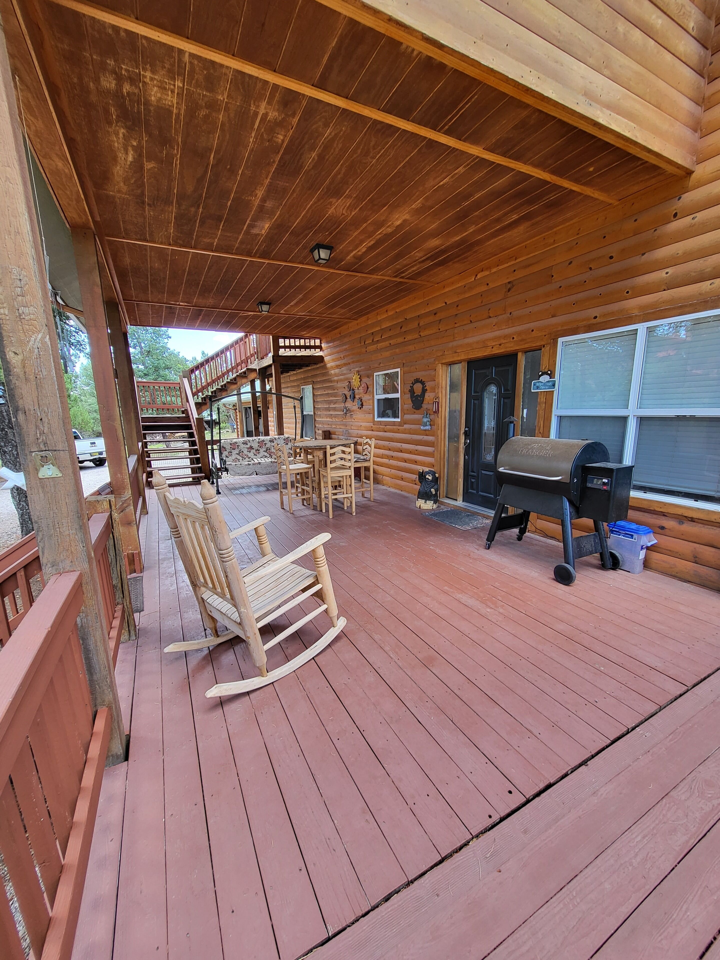 A wooden deck with a covered seating area, a barbecue grill, and a staircase leading to an upper level.