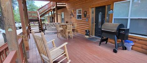 A wooden deck with a covered seating area, a barbecue grill, and a staircase leading to an upper level.