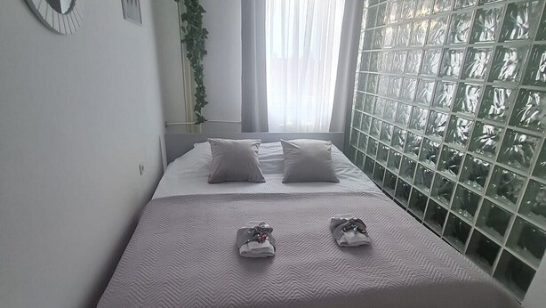 Un dormitorio ordenado con cama, mesita de noche, espejo y ventana con vistas.