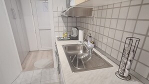 Una cocina compacta con un lavamanos de acero inoxidable, un microondas y una tetera. Hay una ventana pequeña con vistas al exterior.