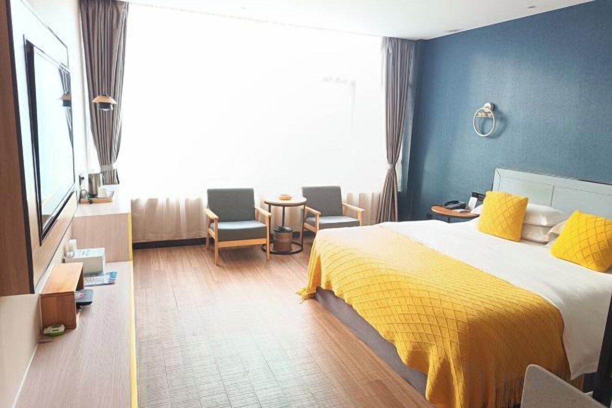 A hotel room with a bed, two armchairs, a small table, a TV, and a window with curtains.