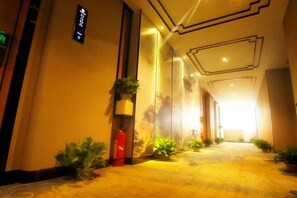 A hotel corridor with a carpeted floor, potted plants, and a fire extinguisher. - Rong'an International Hotel (Rong'an)