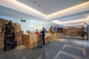 Un espace d’accueil avec un comptoir en bois, une réceptionniste et un visiteur debout.