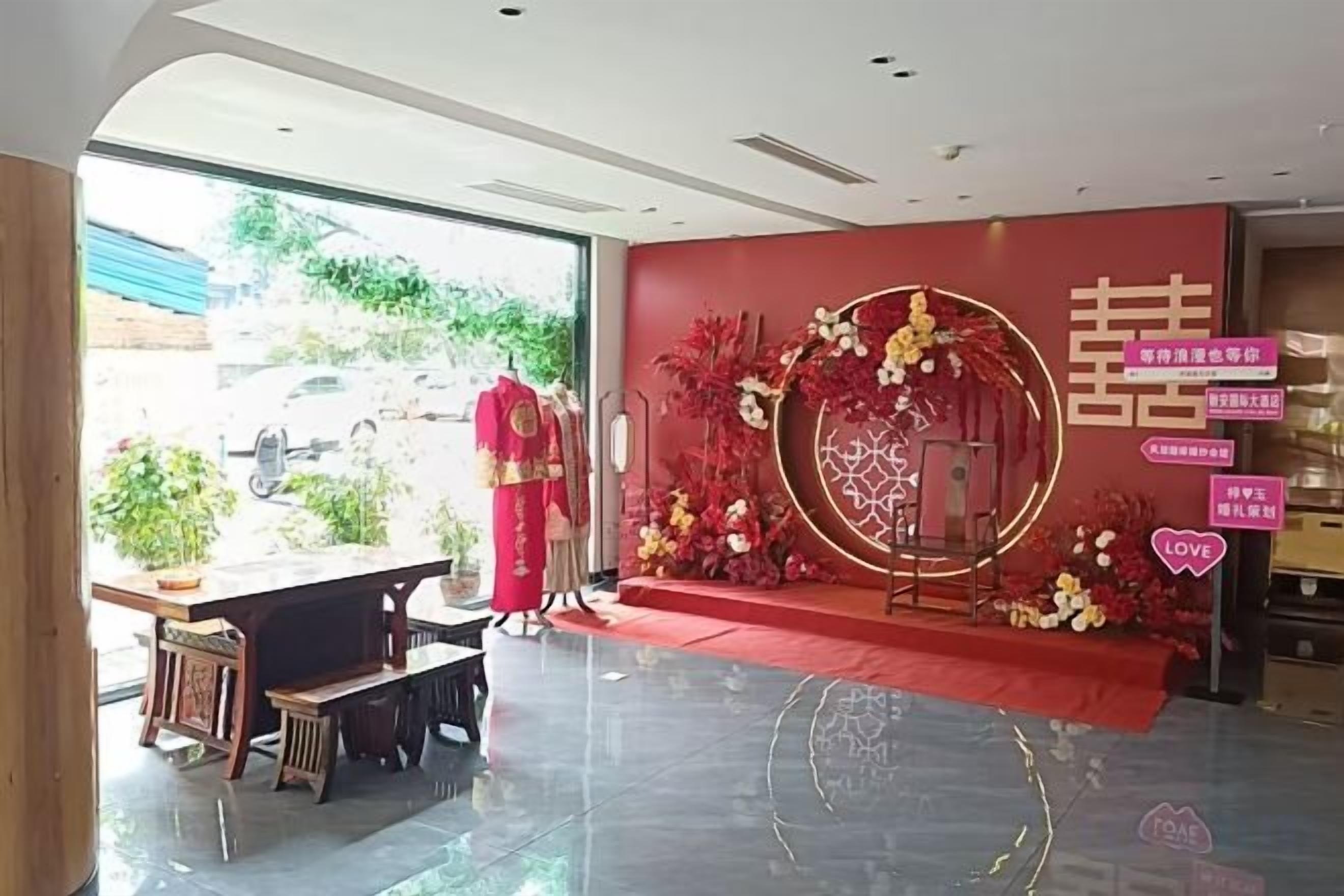 A hotel lobby with a reception desk, a red carpeted area, and a decorative wall with floral patterns.