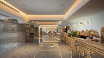 Eine moderne Hotelhalle mit einer Rezeption, einer Sitzgelegenheit und Blick in den Speiseraum.