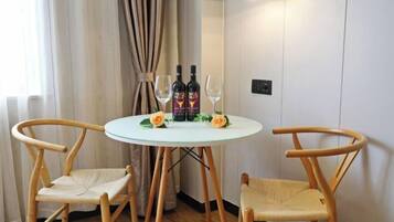 A small round table with two chairs, two bottles of alcohol, and two wine glasses on a white wall.