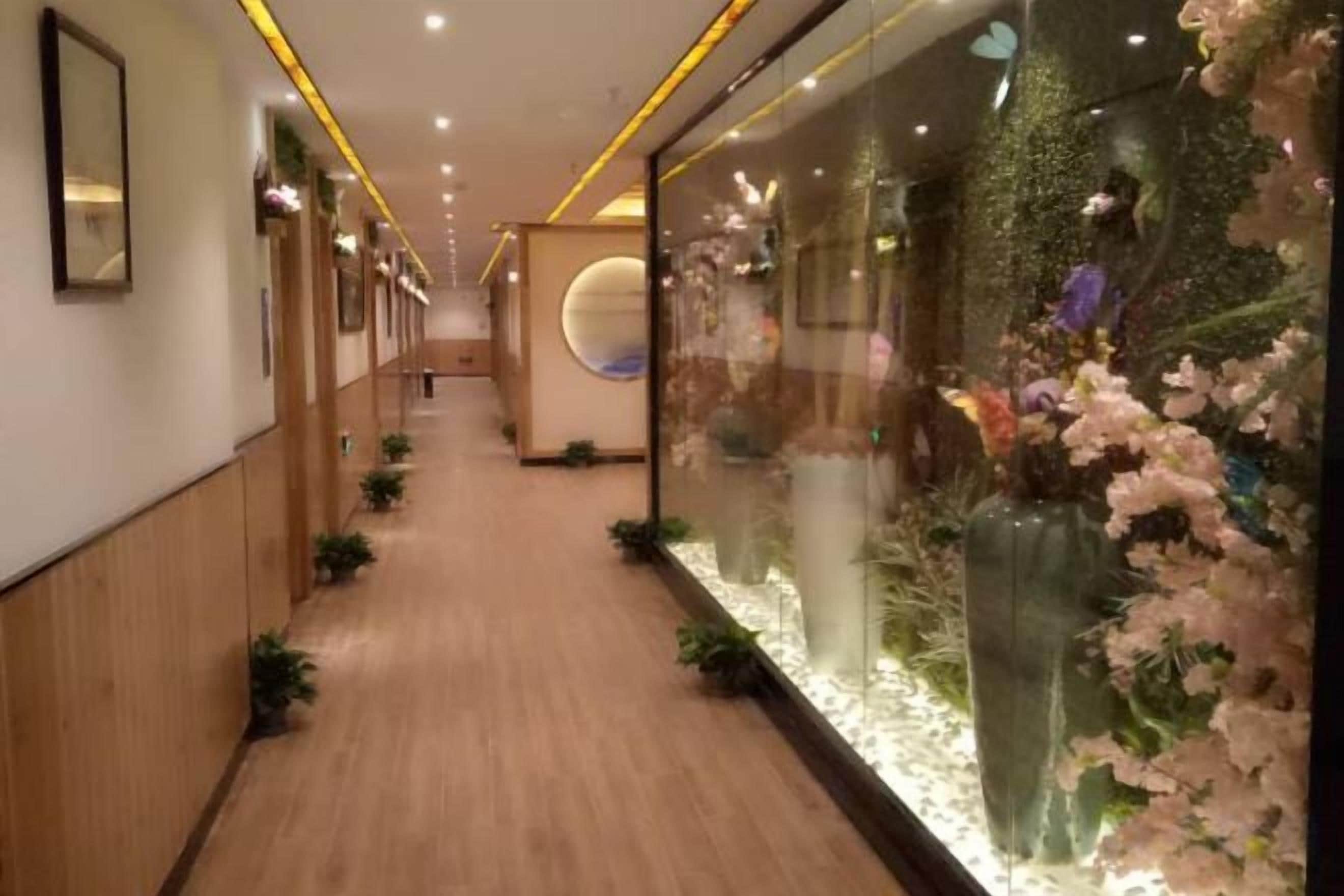A hallway with wooden flooring, glass walls, and decorative floral arrangements.