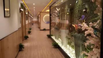 A hallway with wooden flooring, glass walls, and decorative floral arrangements.
