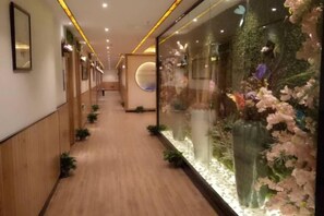 A hallway with wooden flooring, glass walls, and decorative floral arrangements. - Rong'an International Hotel (Rong'an)