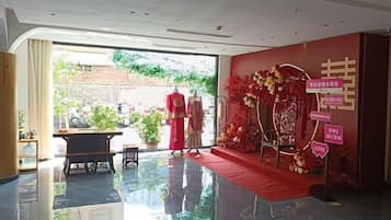 Un hall de hotel con alfombra roja, un escenario con decoración floral y vistas al exterior.