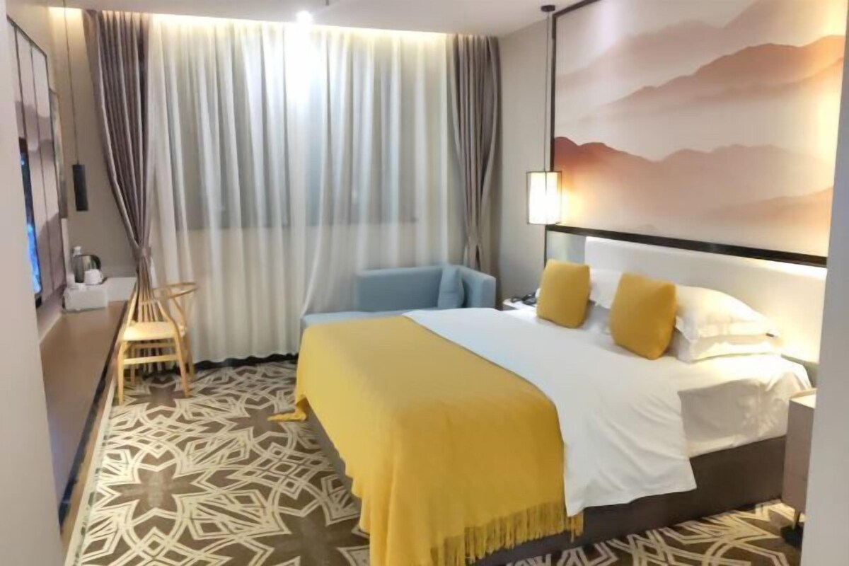 A hotel room with a bed, a chair, a desk, a lamp, and a view of the mountains.