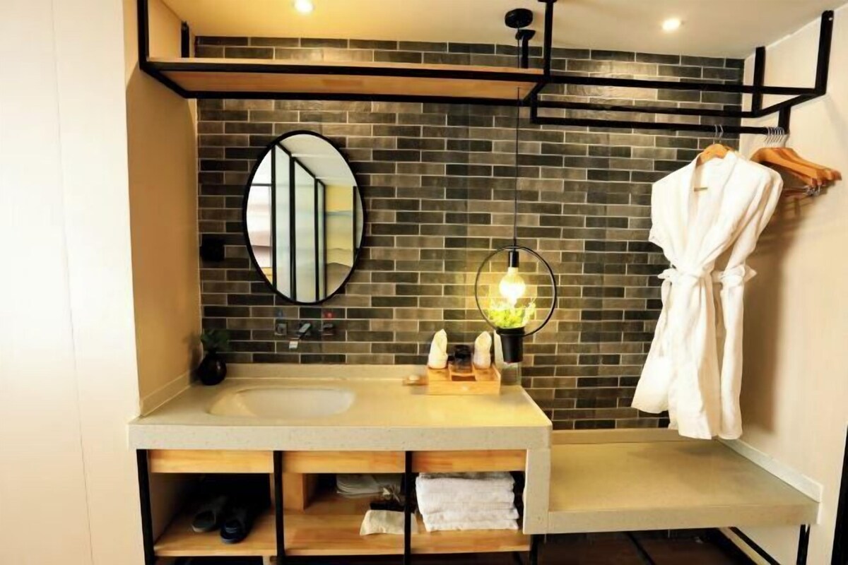 A modern bathroom with a large mirror, a round light fixture, and a robe hanging on a rack.