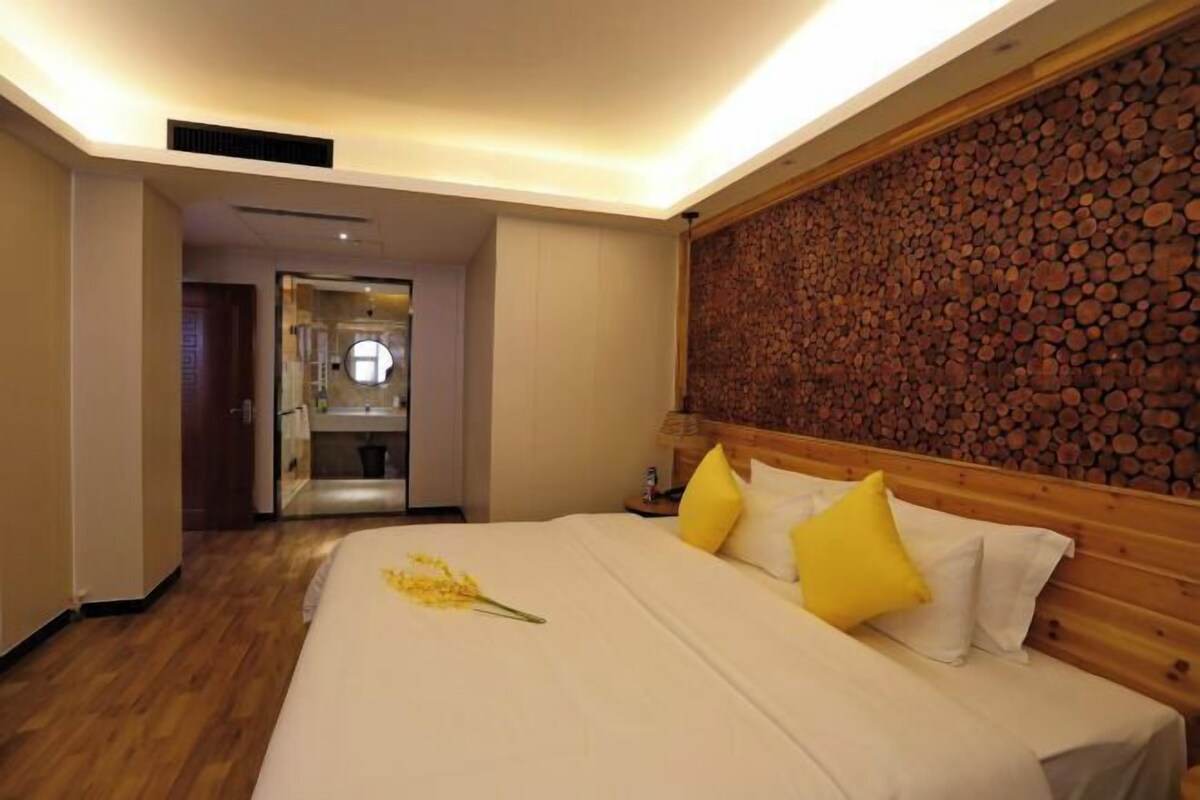 A hotel room with a wooden headboard, a bed with white and yellow bedding, and a wall decorated with stacked logs.