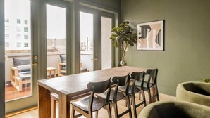 A dining area with a wooden table and chairs, large windows, a plant, and a framed picture on the wall. - King St. Manor | Luxury Penthouse - King St Views! (Charleston)