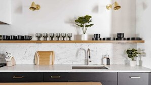 A modern kitchen with a marble countertop, a sink, and a wooden shelf above it. - King St. Manor | Luxury Penthouse - King St Views! (Charleston)