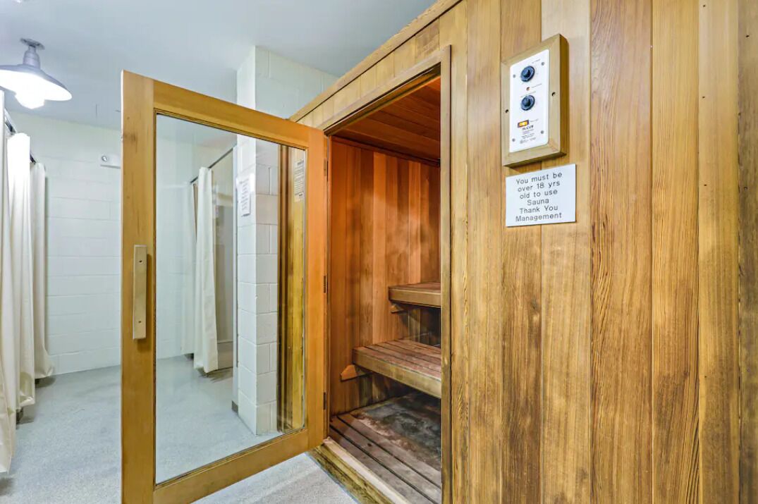A sauna room with wooden walls, a wooden bench, and a control panel. There is a sign indicating age restriction.