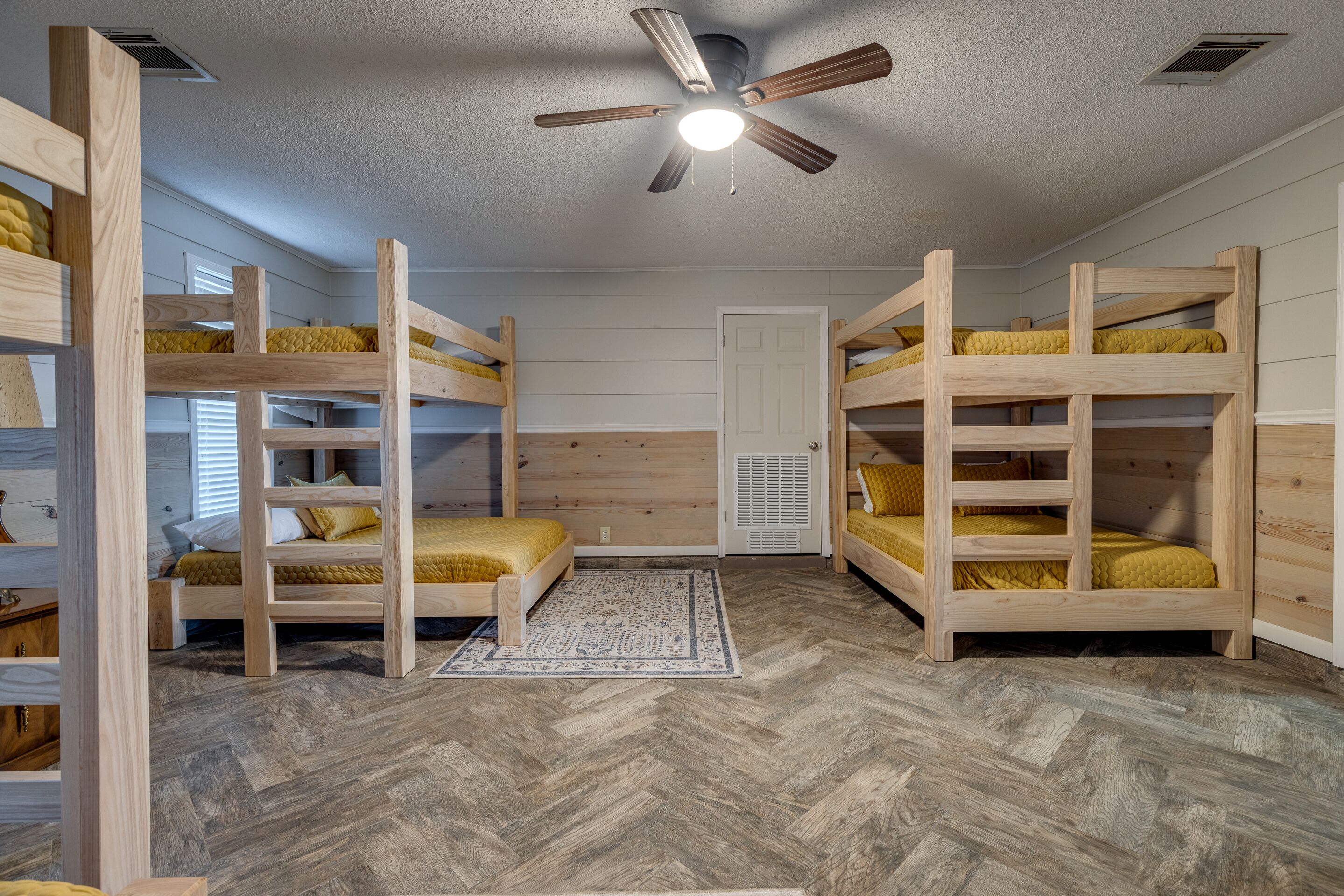 A room with bunk beds, a ceiling fan, and a patterned rug.