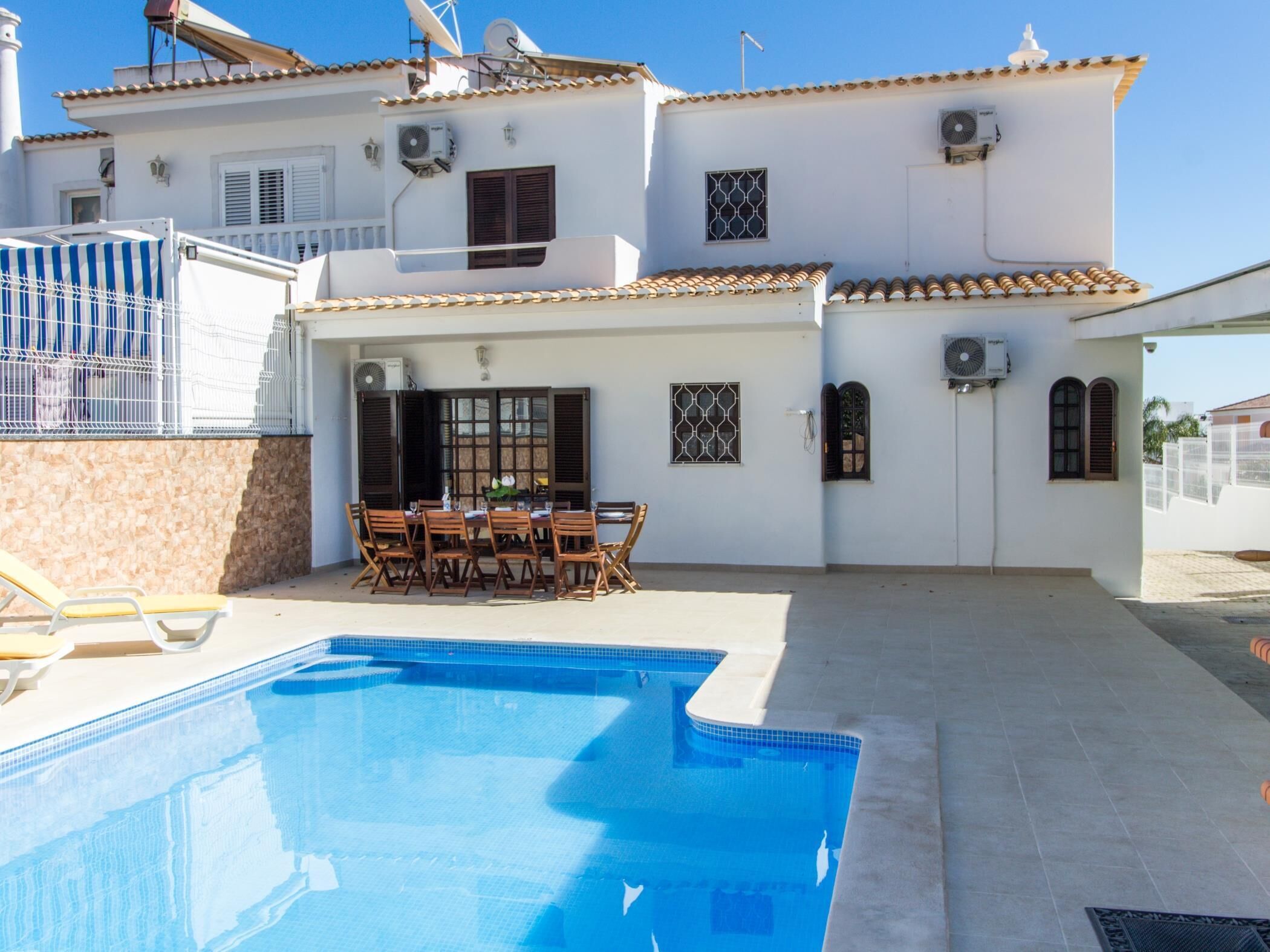 A two-story building with a swimming pool, outdoor seating, and multiple air conditioning units.