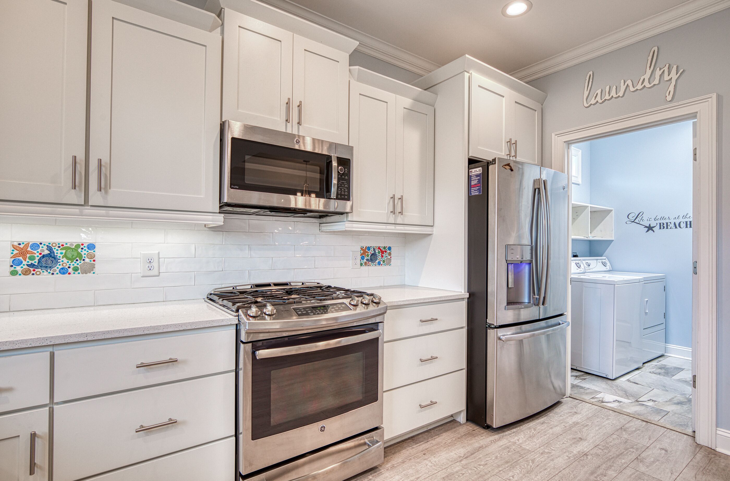 A modern kitchen with stainless steel appliances, white cabinetry, and a laundry area.