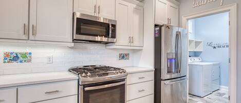 A modern kitchen with stainless steel appliances, white cabinetry, and a laundry area.