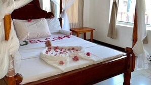Una cama con dosel, sábanas blancas y decoración floral rosa.