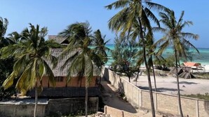 Escena de playa con palmeras, una construcción de techo de paja y cielo azul despejado.