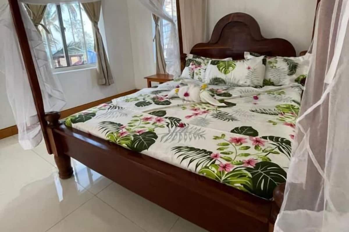 Una cama con dosel, un edredón floral, un cabecero de madera y cortinas de gasa.