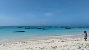 Una playa con barcos en el agua y una persona de pie sobre la arena.