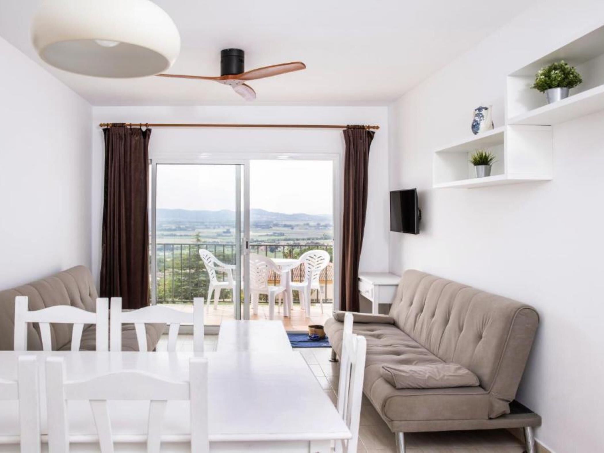Un salon moderne comprenant un coin repas, un canapé, un téléviseur fixé au mur et un balcon offrant une vue sur la campagne.