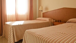 Een hotelkamer met twee bedden, een nachtkastje, een lamp en een raam met gordijnen.