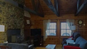 Ein gemütlicher Blockhausszimmer mit Steinwand, Holzbalken, Kamin, Fernseher und einer Couch.
