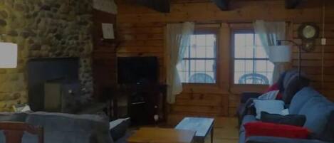 Une pièce confortable, aménagée comme un chalet, avec un mur en pierre, des poutres en bois, une cheminée, une télévision et un canapé.