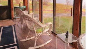 Eine Holzterrasse mit Schaukelstühlen und einem Tisch, mit Blick auf eine Rasenfläche und ein Gewässer.
