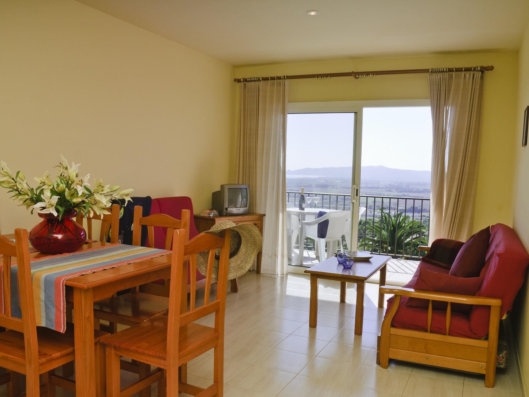 A living room with a dining table, chairs, a TV, and a balcony with a view.