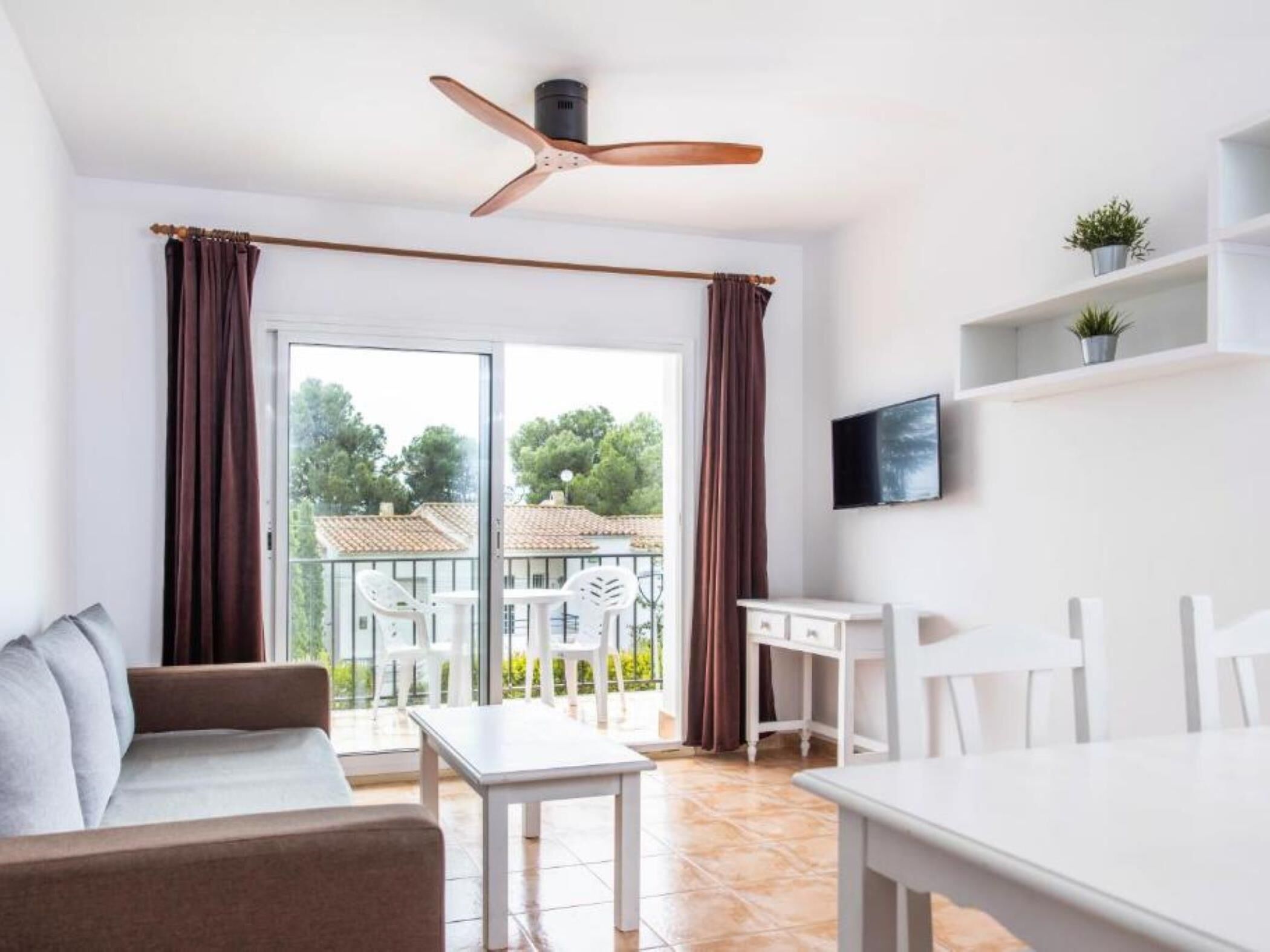 A modern room with a sliding glass door to a balcony, a ceiling fan, a white desk, and a sofa.