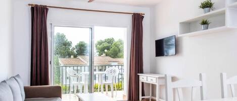 A modern room with a sliding glass door to a balcony, a ceiling fan, a white desk, and a sofa.