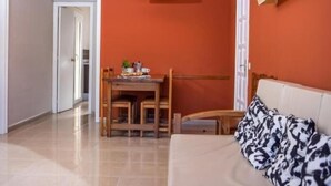 A room with a sofa, a dining table with chairs, and a hanging light fixture. - APCOSTAS Tropik / a bedrooms (L'Estartit)