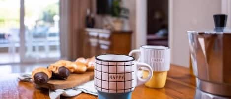 A kitchen with a coffee maker, two mugs, and a wooden table.