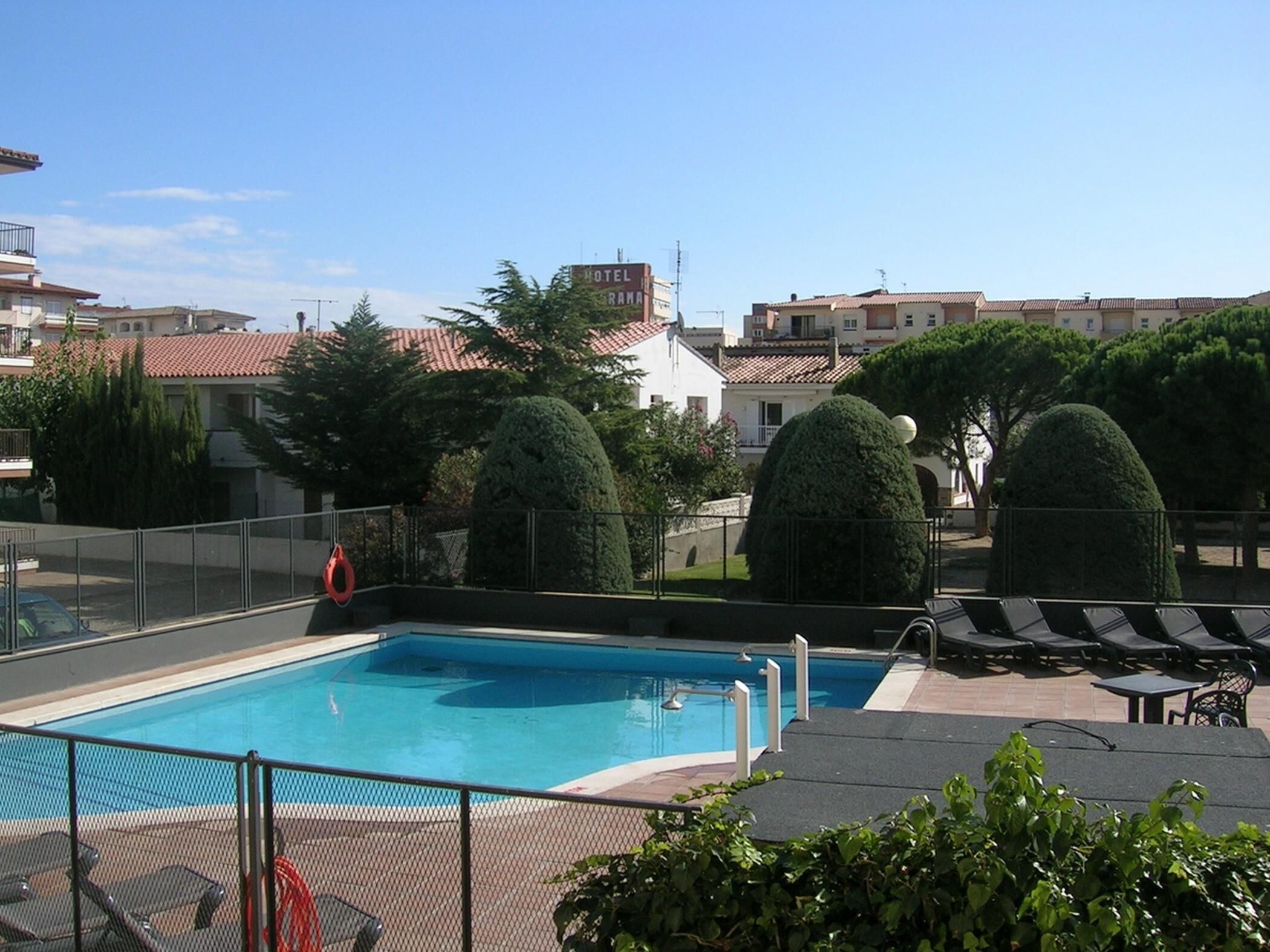 A swimming pool with a fenced area, lounge chairs, and neatly trimmed bushes.