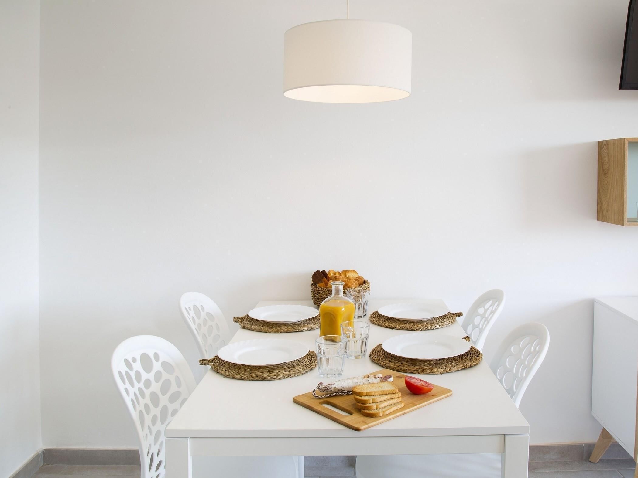 A dining table with white chairs, a white tablecloth, and a basket of bread.