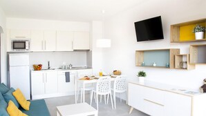 A modern kitchen with white cabinets, a microwave, and a dining area with white chairs and a table. - APCOSTAS Estartit Confort / Two Bedrooms (L'Estartit)