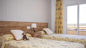 Een hotelkamer met twee bedden, een houten hoofdeinde, een nachtkastje met lamp en uitzicht naar buiten door een schuifdeur.