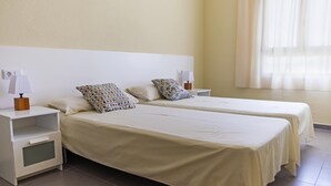 A hotel room with two single beds, each with a white headboard, a bedside table with a lamp, and a nightstand.