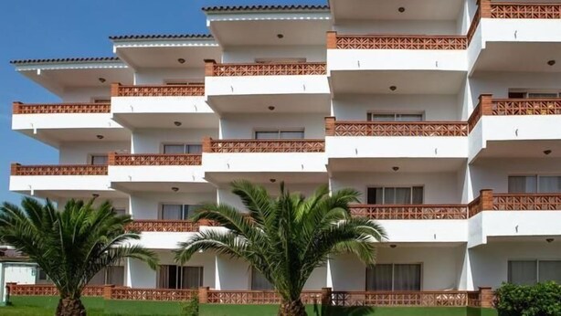 A multi-story hotel with balconies, palm trees, and a clear blue sky. - APCOSTAS Quijote / Un Dormitorio (L'Estartit)