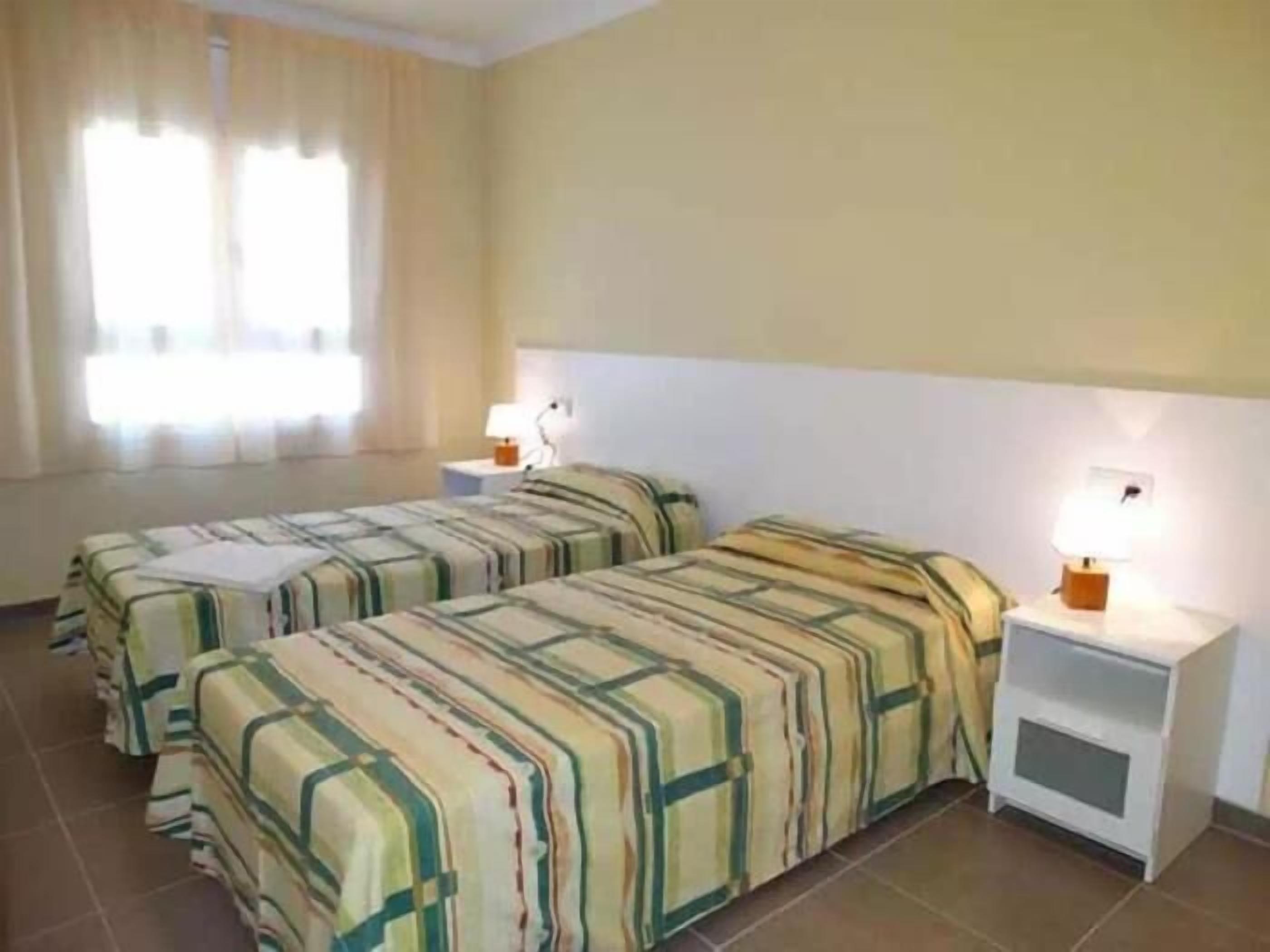 Une chambre d’hôtel avec deux lits, chacun recouvert d’une couvre-lit à rayures, une table de chevet avec une lampe et une fenêtre avec des rideaux.