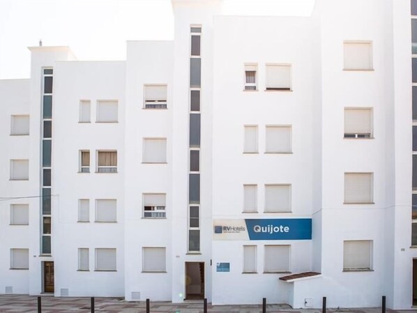 Un hôtel à plusieurs étages, doté d’une façade blanche, de nombreuses fenêtres et d’une enseigne indiquant « RV Hotels Quijote ».