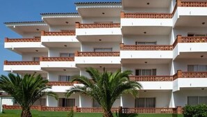 Un hôtel à plusieurs étages, doté de balcons, de palmiers et surplombant un ciel d’un bleu limpide.